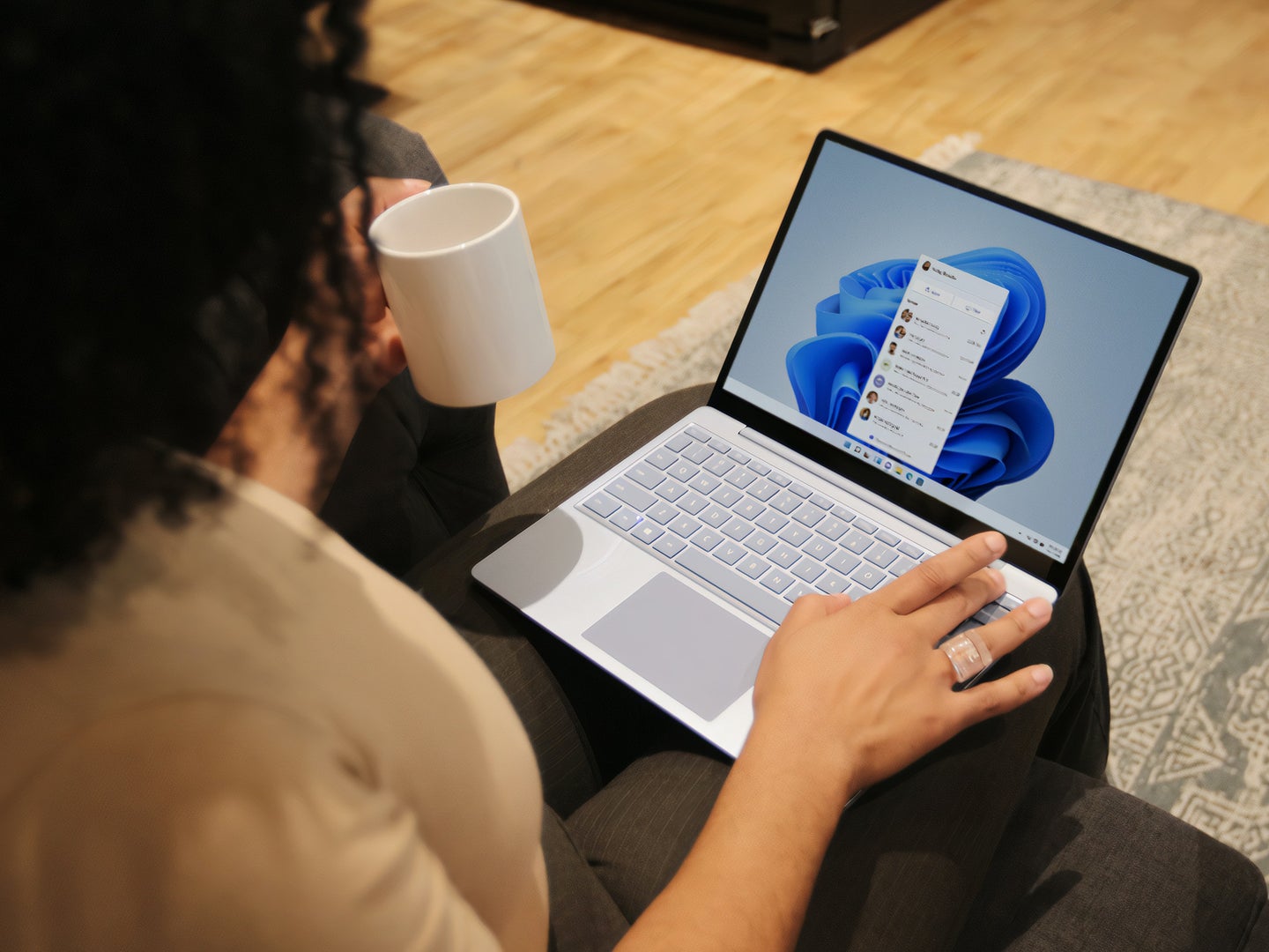 Black person sitting with surface laptop their lap while holding a mug