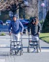 Two patients with paralysis walking down a sidewalk with aides after electrode therapy