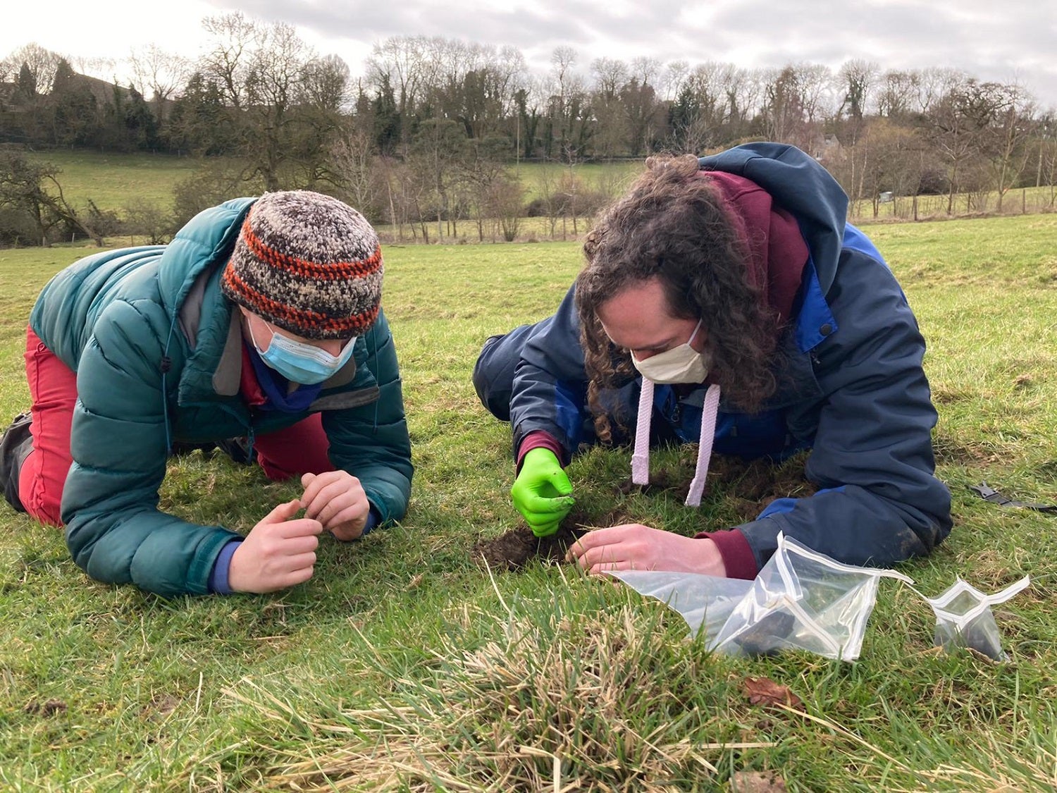 Scientists in hats and jackets laying in a field looking at meteorite fragments