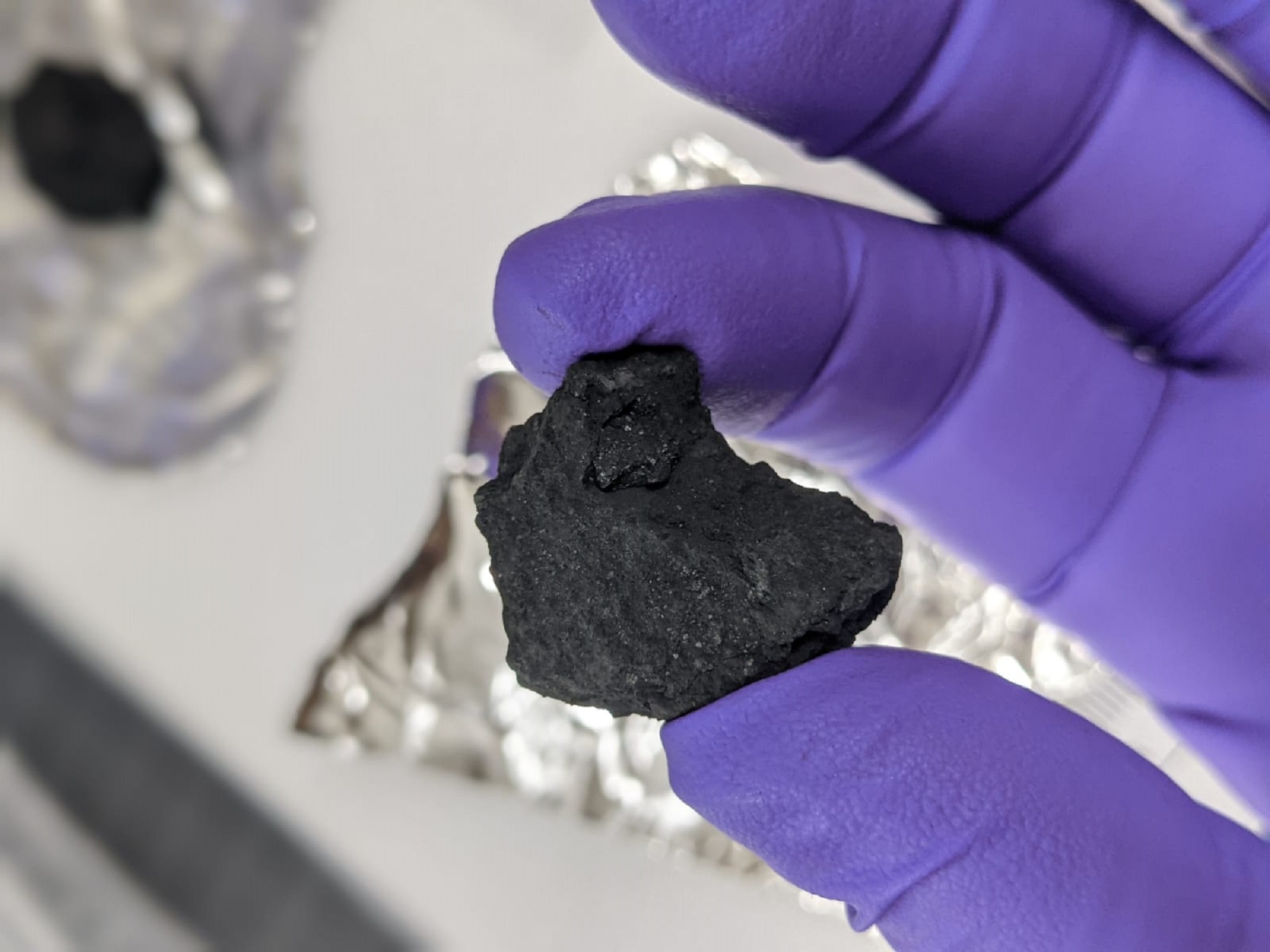 Winchcombe meteorite fragment in a purple-gloved hand for chemical analysis