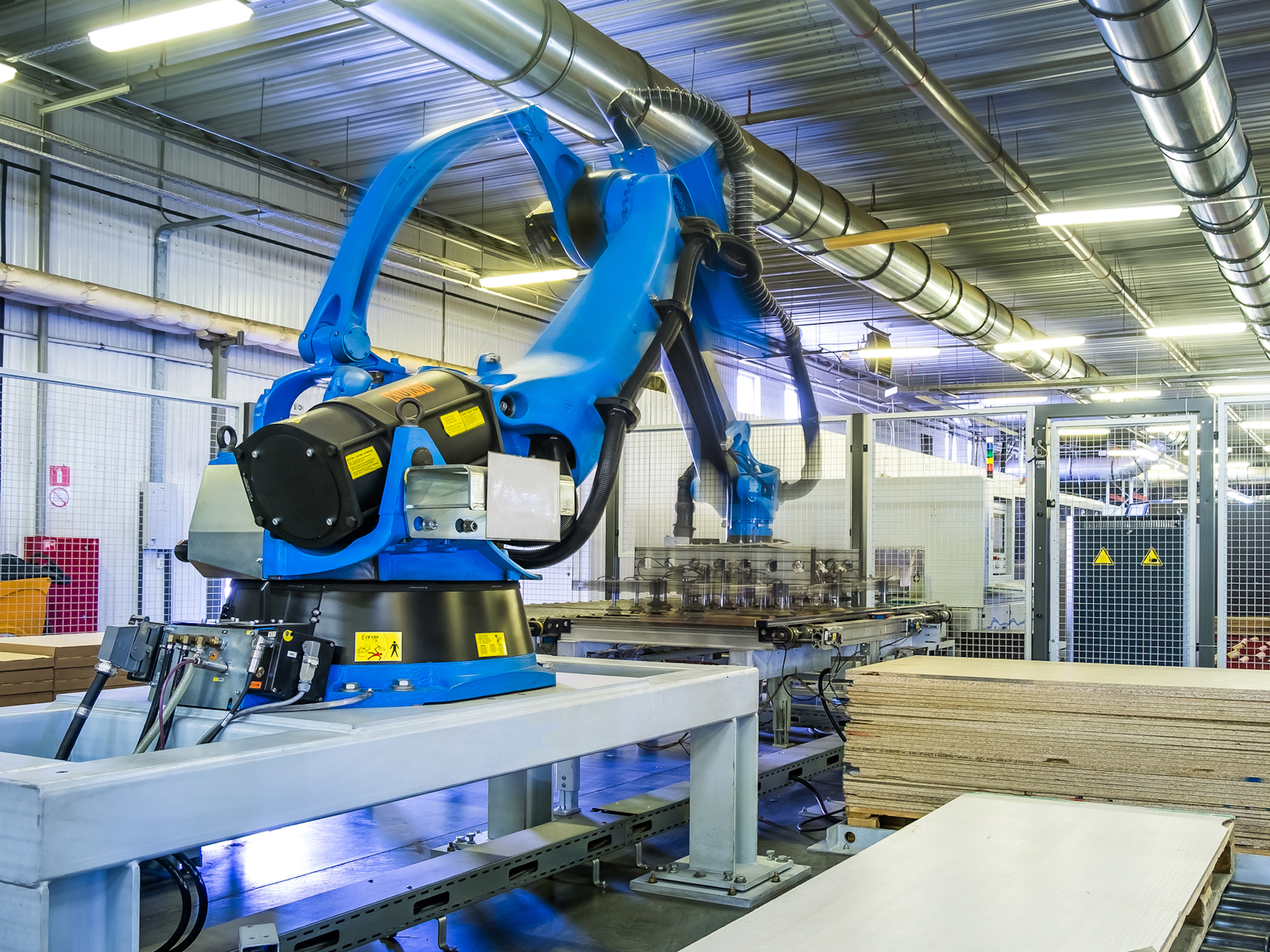 Blue robotic arm in factory working on assembly line with plywood materials