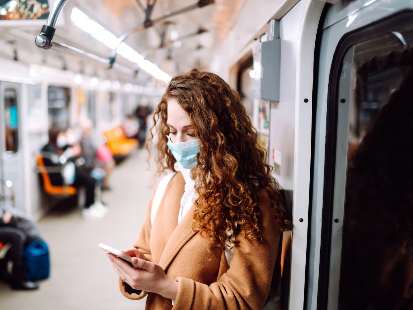 Woman wearing face mask while looking at phone while standing in subway car