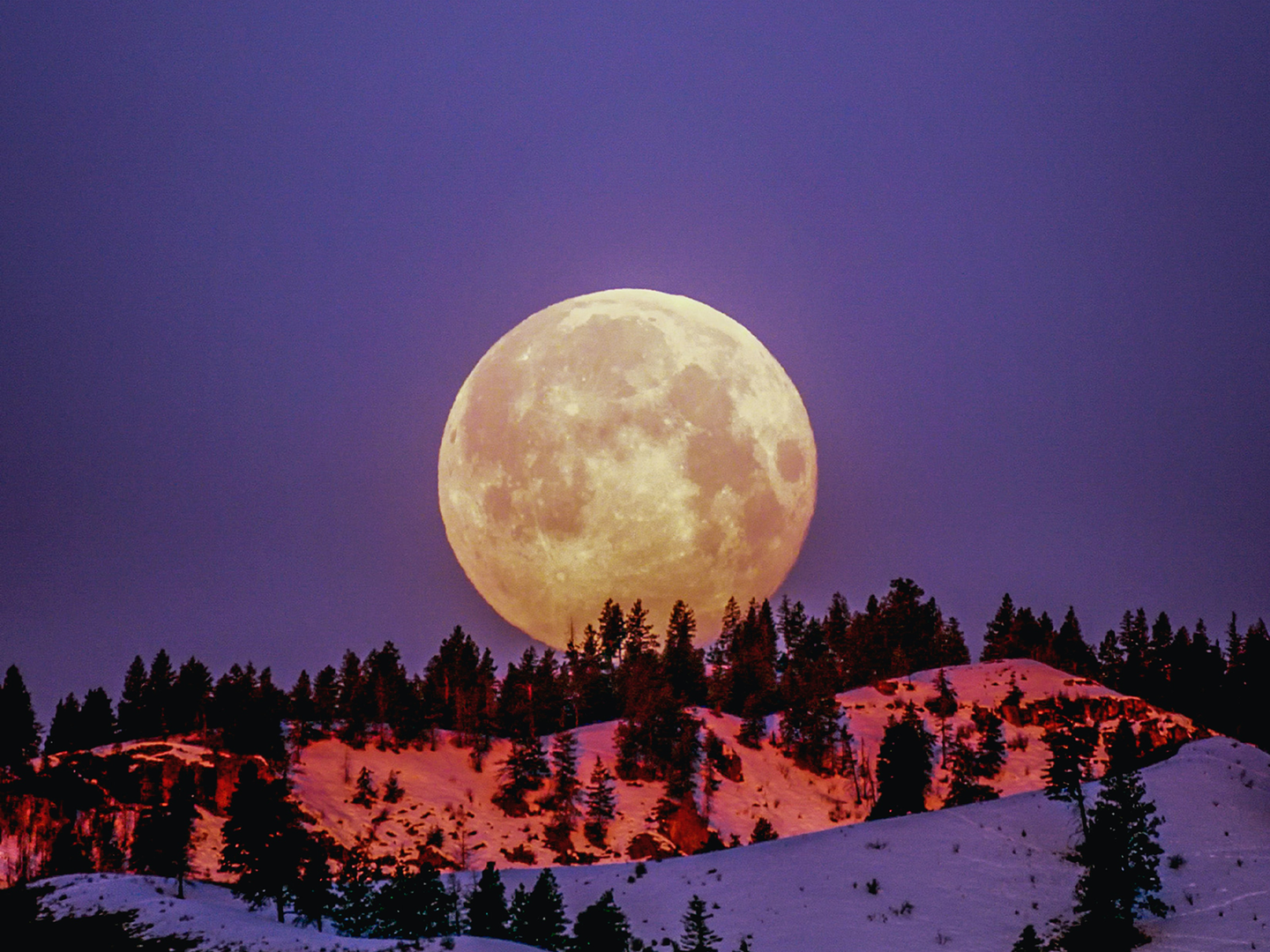 A full moon rises over snowy hills.