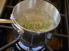 pot with boiling water and sprig of rosemary boiling over a kitchen stove