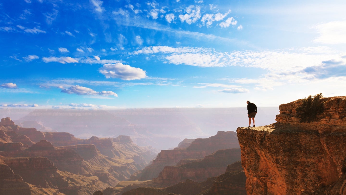 Man standing on ledge overlooking Grand Canyon on a sunny day