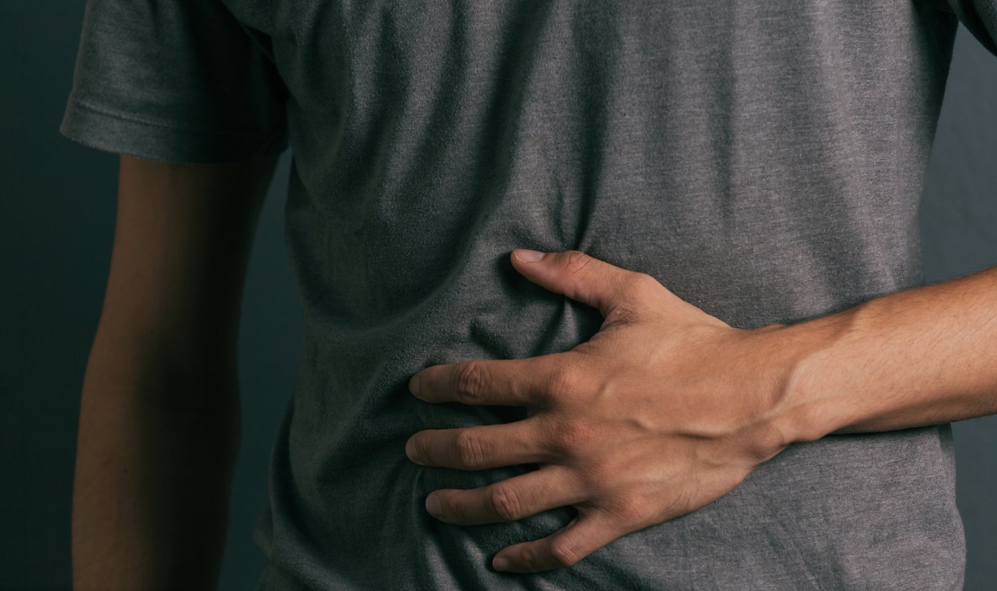 a person in a gray shirt their hand over their stomach under dark lighting