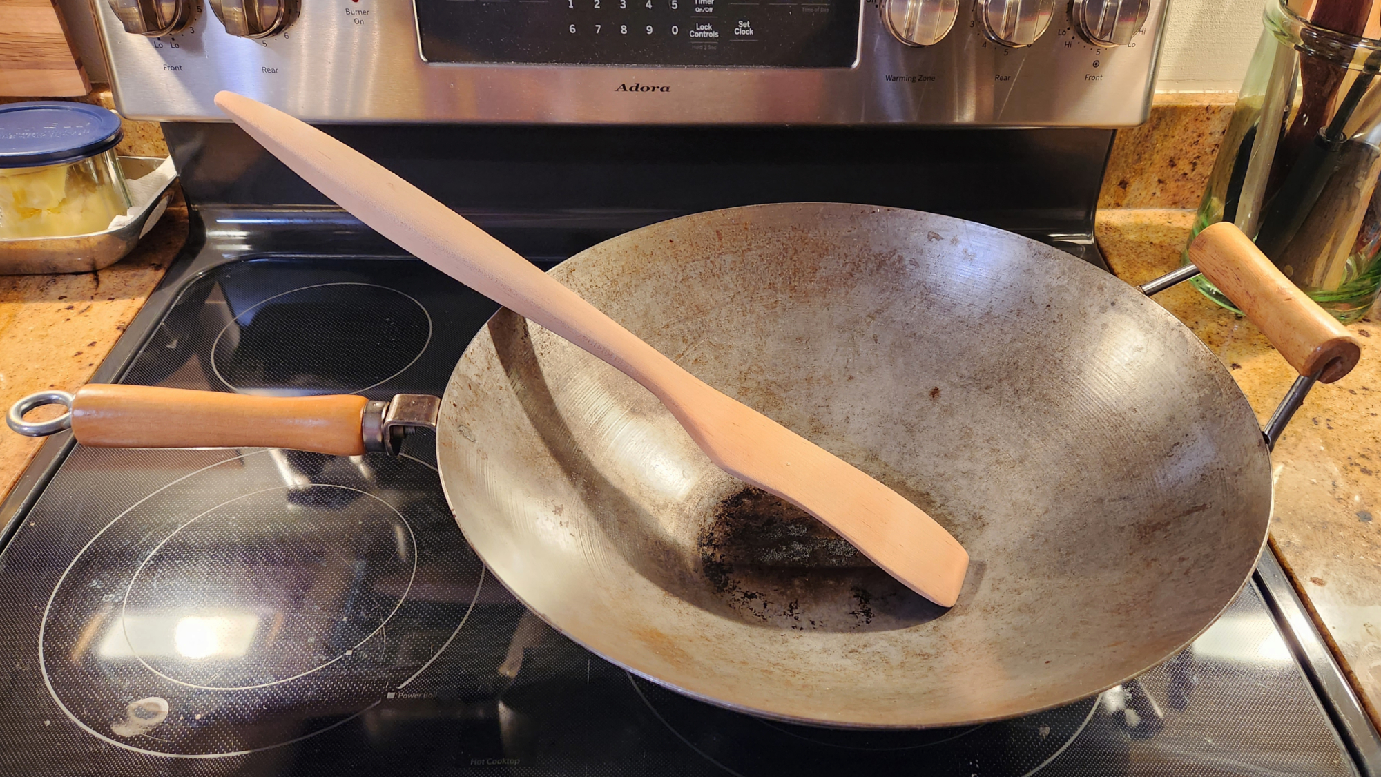 A homemade wooden spoon or spatula inside an empty wok on a black electric stove.
