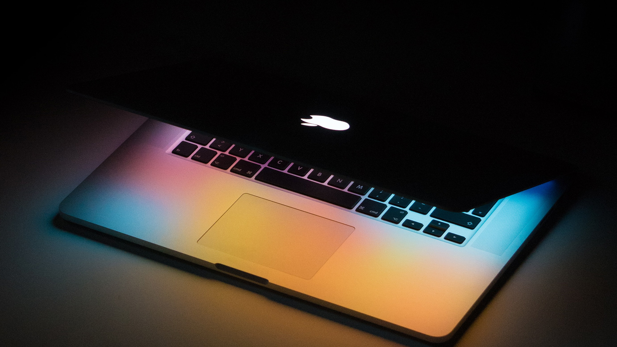 slightly-closed-mac-laptop-on-a-desk-in-a-dark-room
