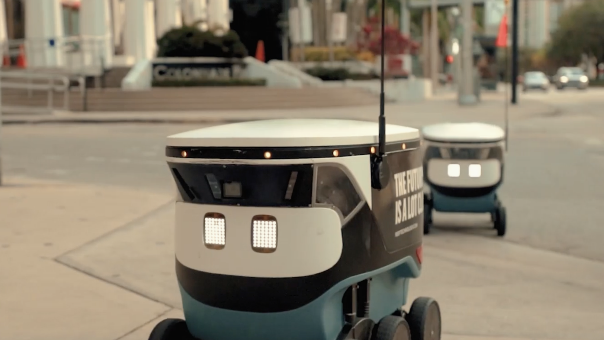 Two Cartken robotic delivery vehicles traveling along a sidewalk in a line