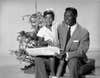 Nat King Cole and his daughter Natalie Cole in front of a Christmas tree singing Christmas songs. Black and white photo.