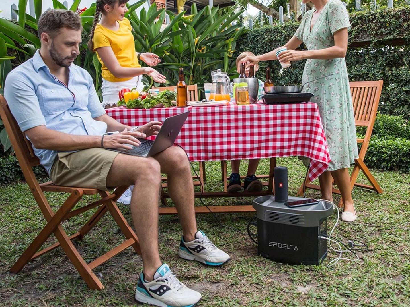 A person using their laptop powered by an electric generator during a picnic
