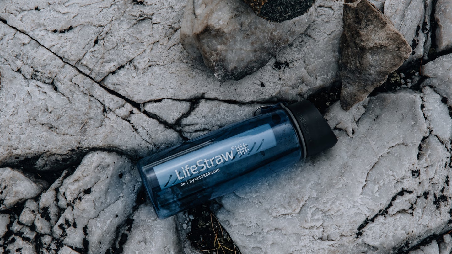 A LifeStraw water filter and bottle on some gray rocks.