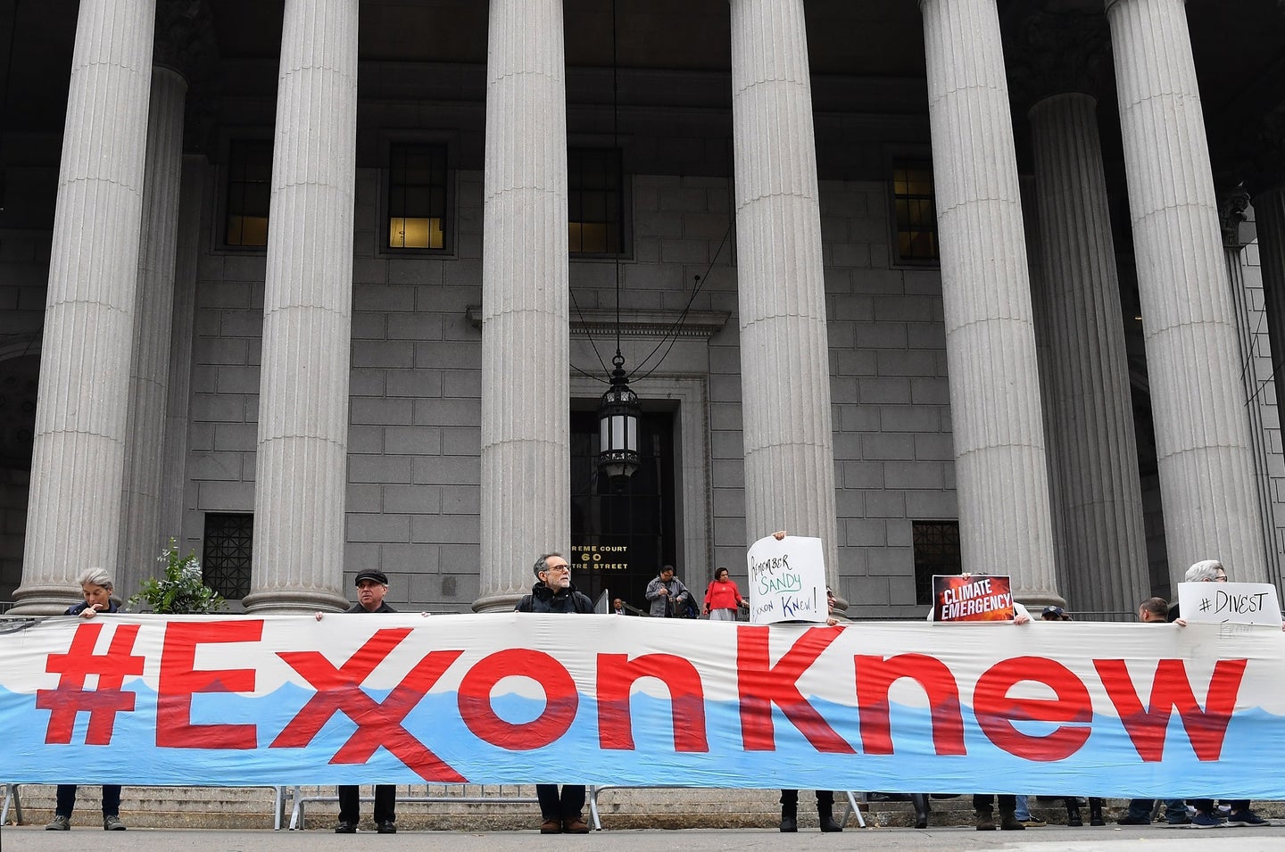 People stand in front of a courthouse holding up a large banner reading #ExxonKnew