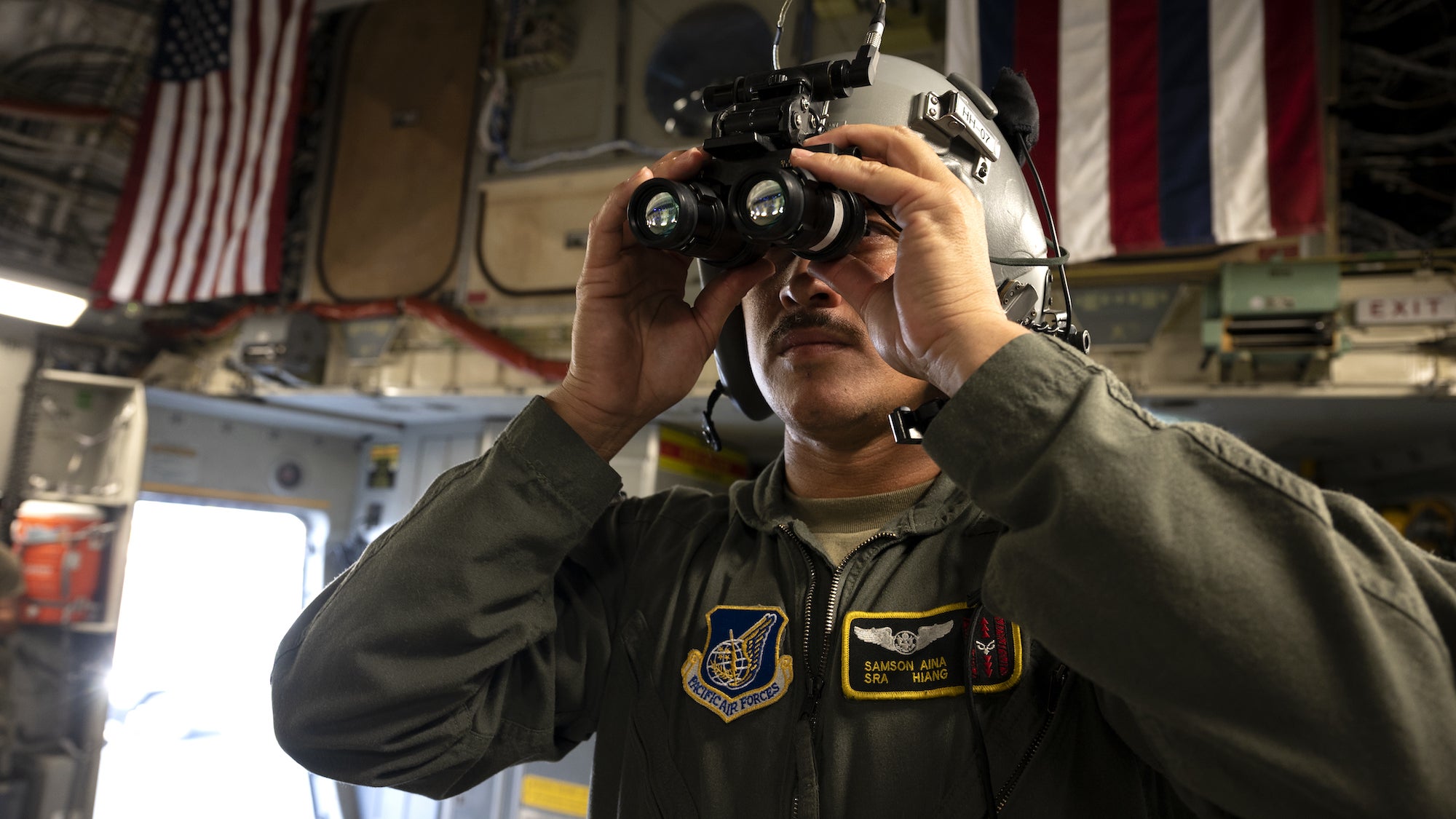 A member of the Hawaii Air National Guard holding night vision goggles up to his eyes.