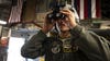 A member of the Hawaii Air National Guard holding night vision goggles up to his eyes.