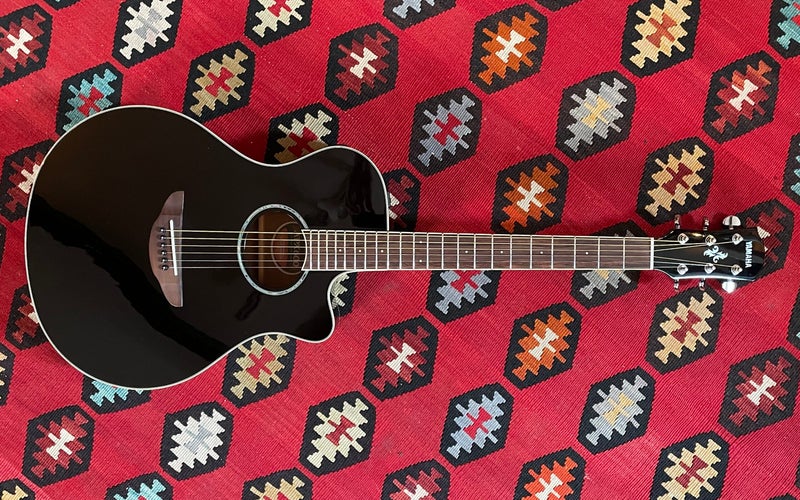 A black Yamaha APX6000 electric-acoustic guitar flat on a colorful red Southwestern rug