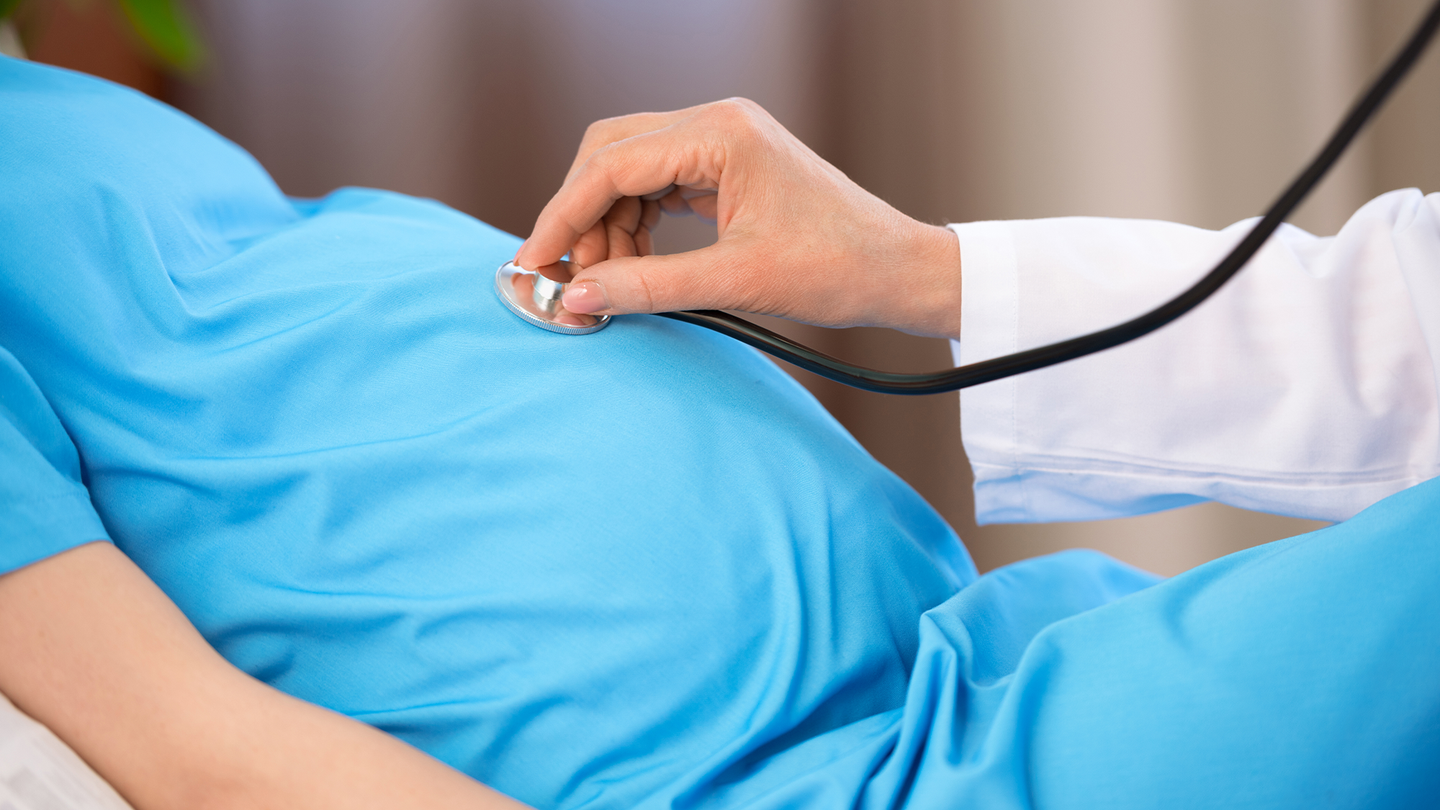 A doctor using a stethoscope to listen to a pregnant person's stomach.