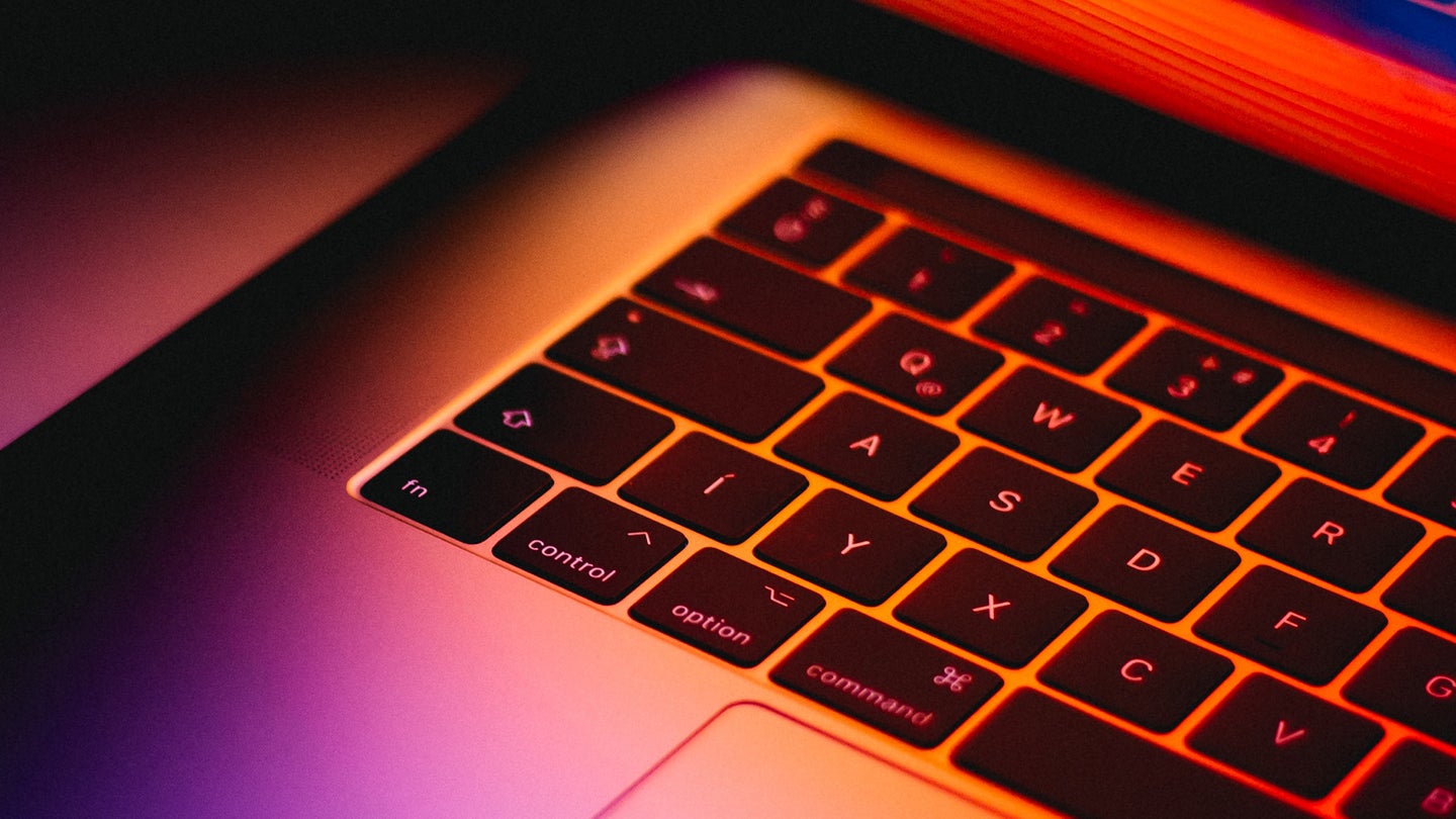 A Macbook keyboard illuminated by red, orange, and purple light.