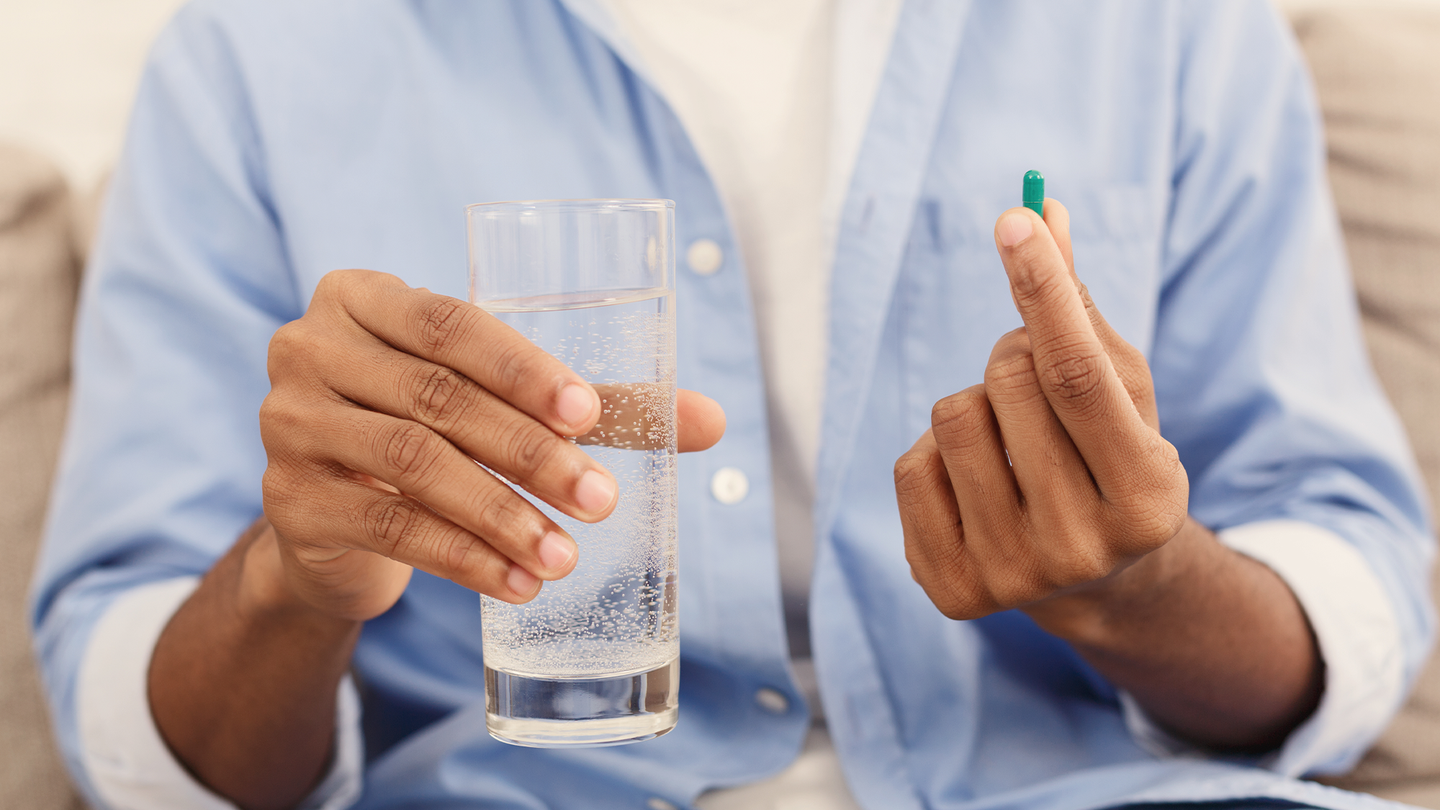 A man holds a brightly colored pill with a glass of water.
