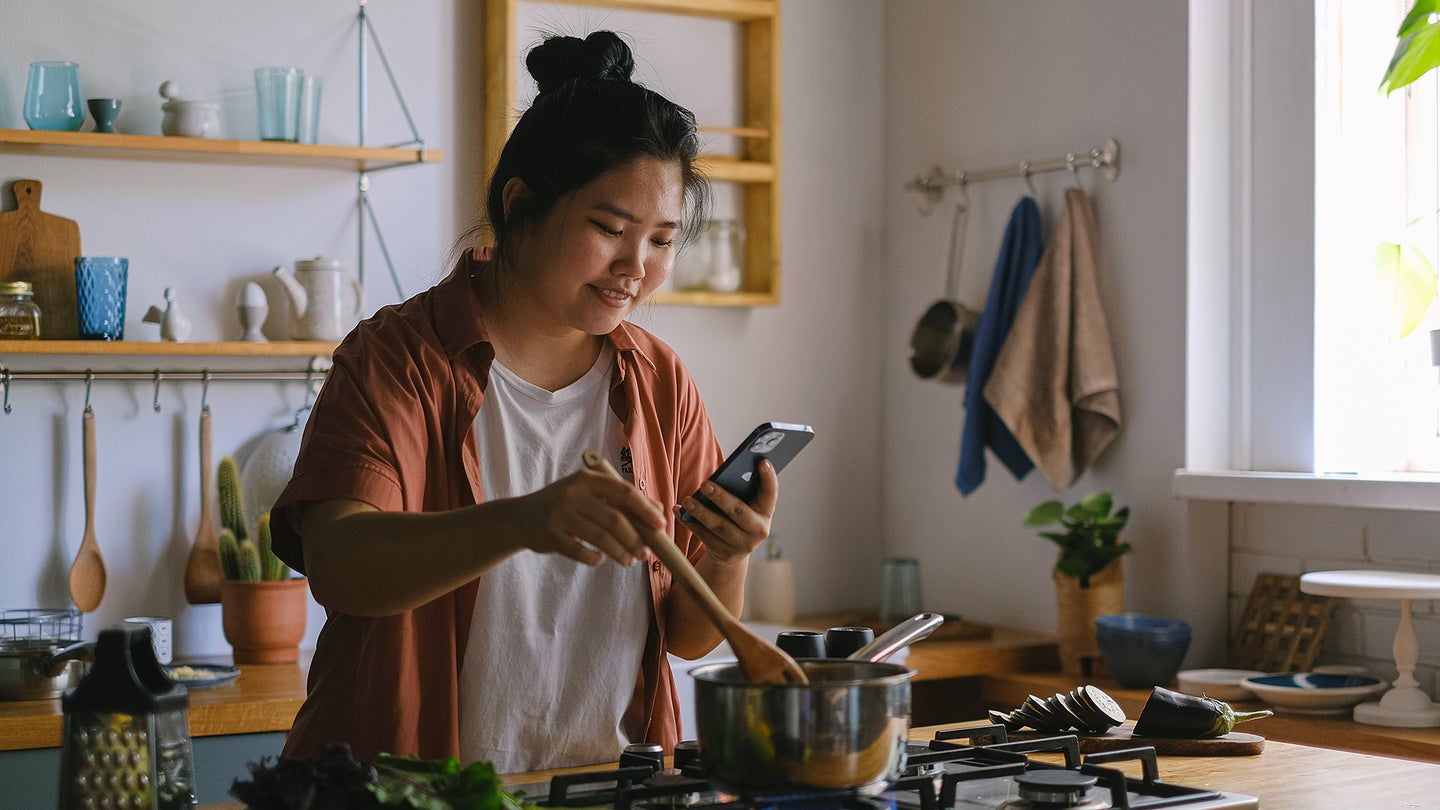 person stirring pot on the stove at the same time as they look at their phone
