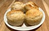 plate of four muffins sitting on a wooden kitchen counter