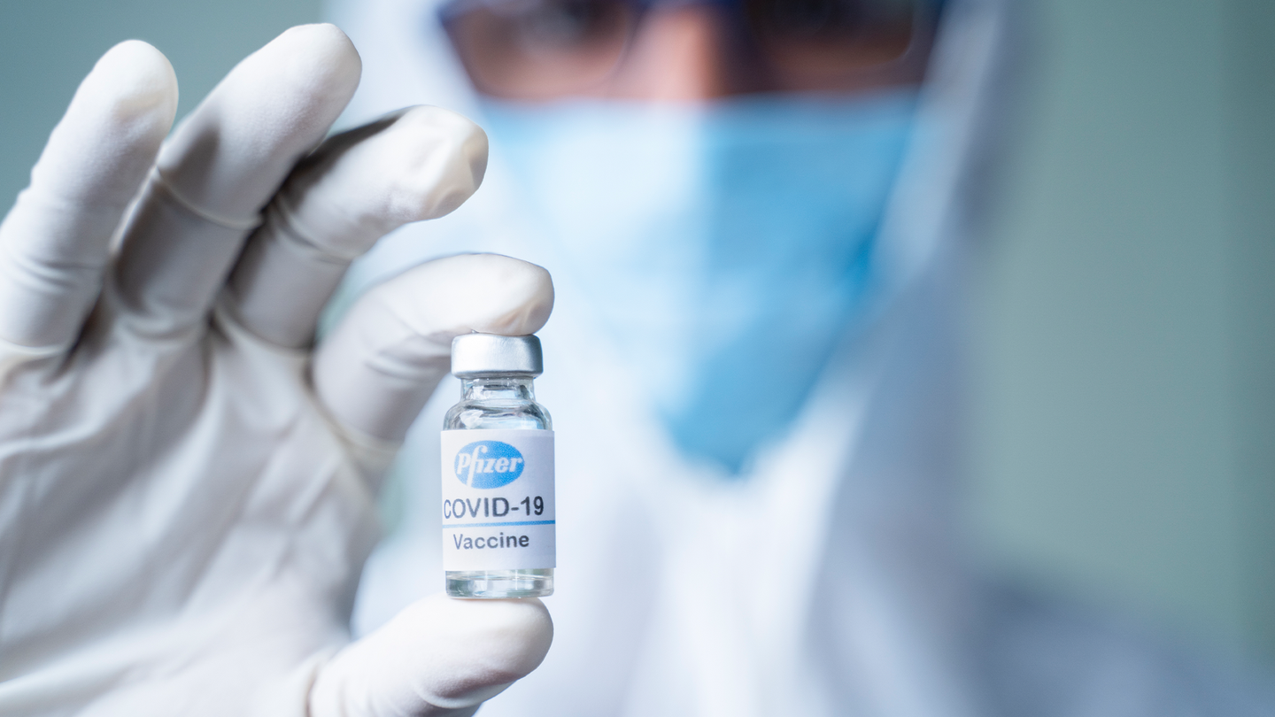 A doctor in a surgical mask holding a vial of Pfizer/BioNTech's COVID-19 vaccine.