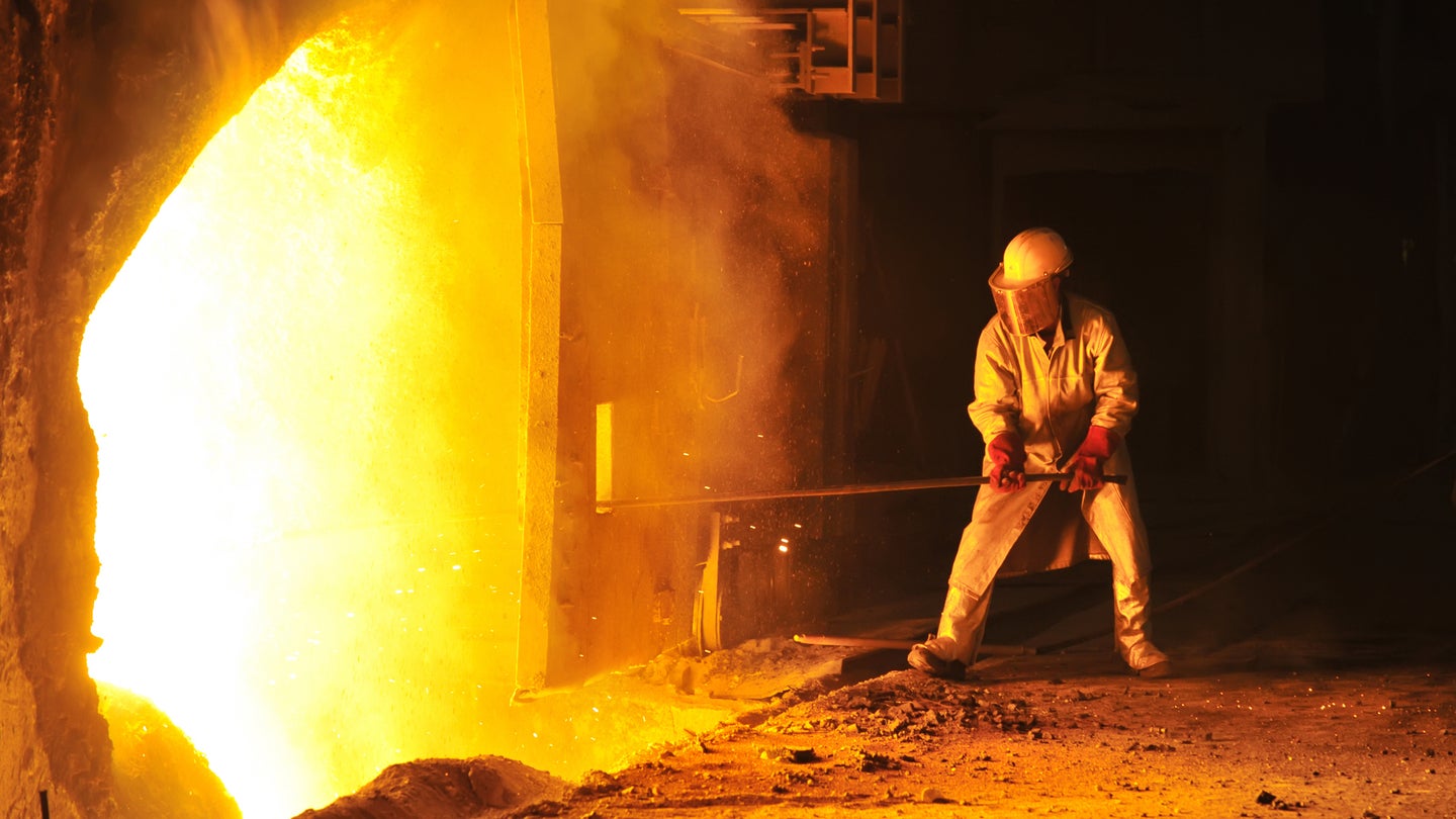 Worker in protective gear takes a sample at steel furnace