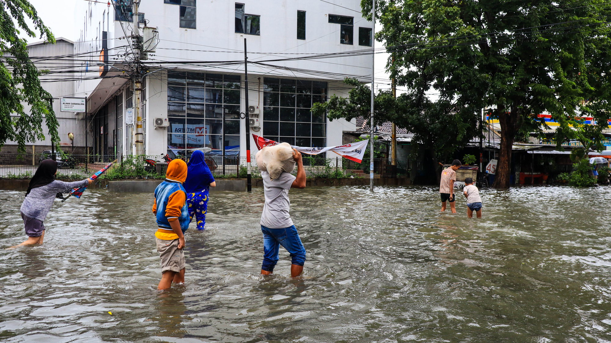 Several people are carrying sacks filled with food and clothing to prepare for evacuation after their house was flooded in Indonesia