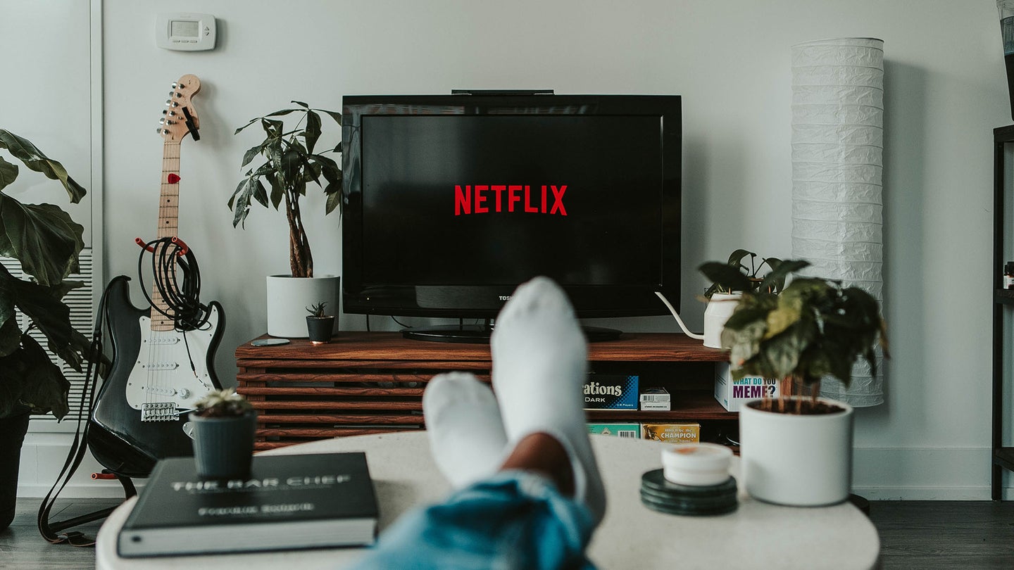 A first-person view of a television loading Netflix as a person puts their legs on a coffee table.