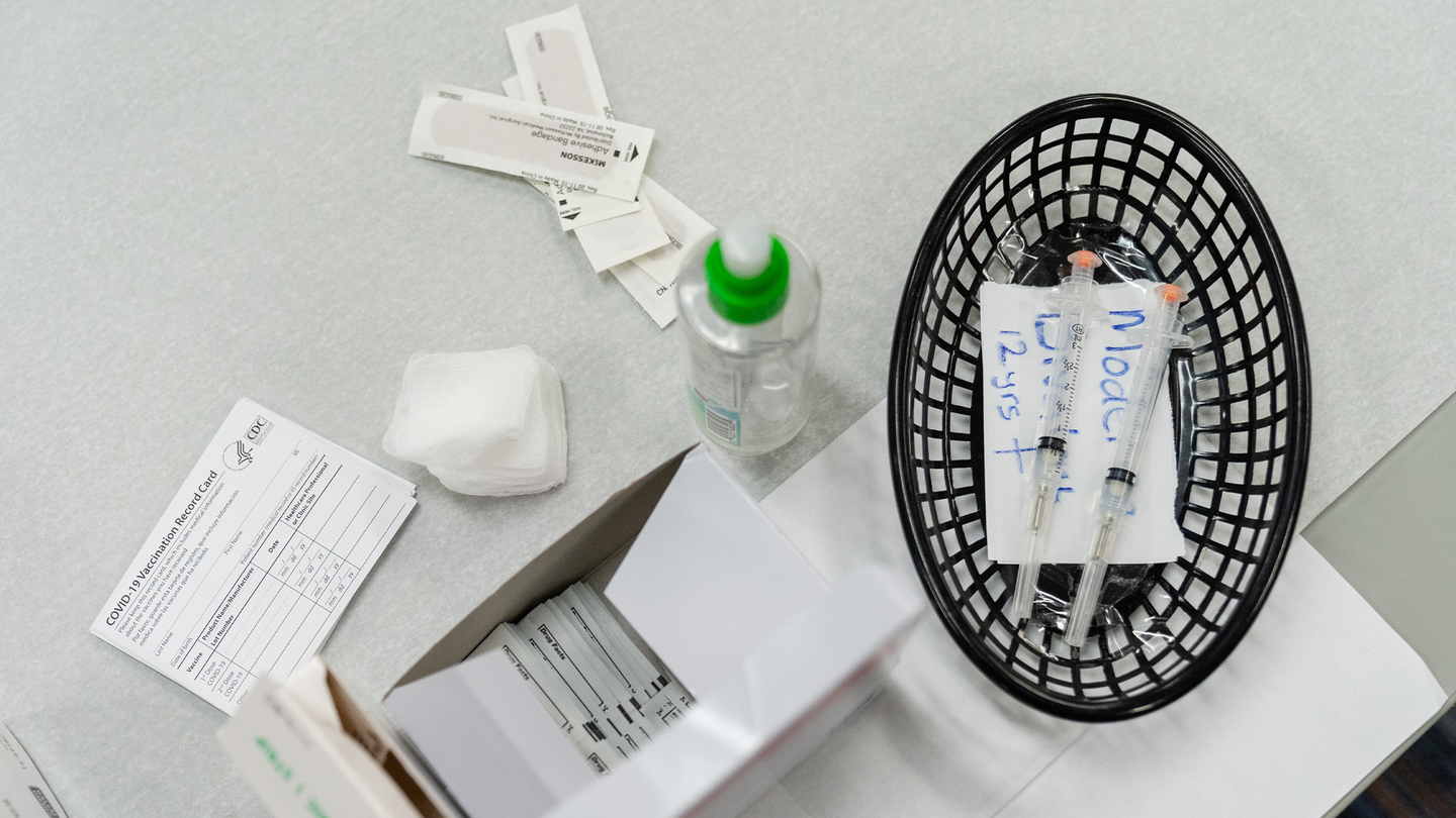 Syringes with the Moderna COVID-19 vaccine on a table with bandaids and a fan.