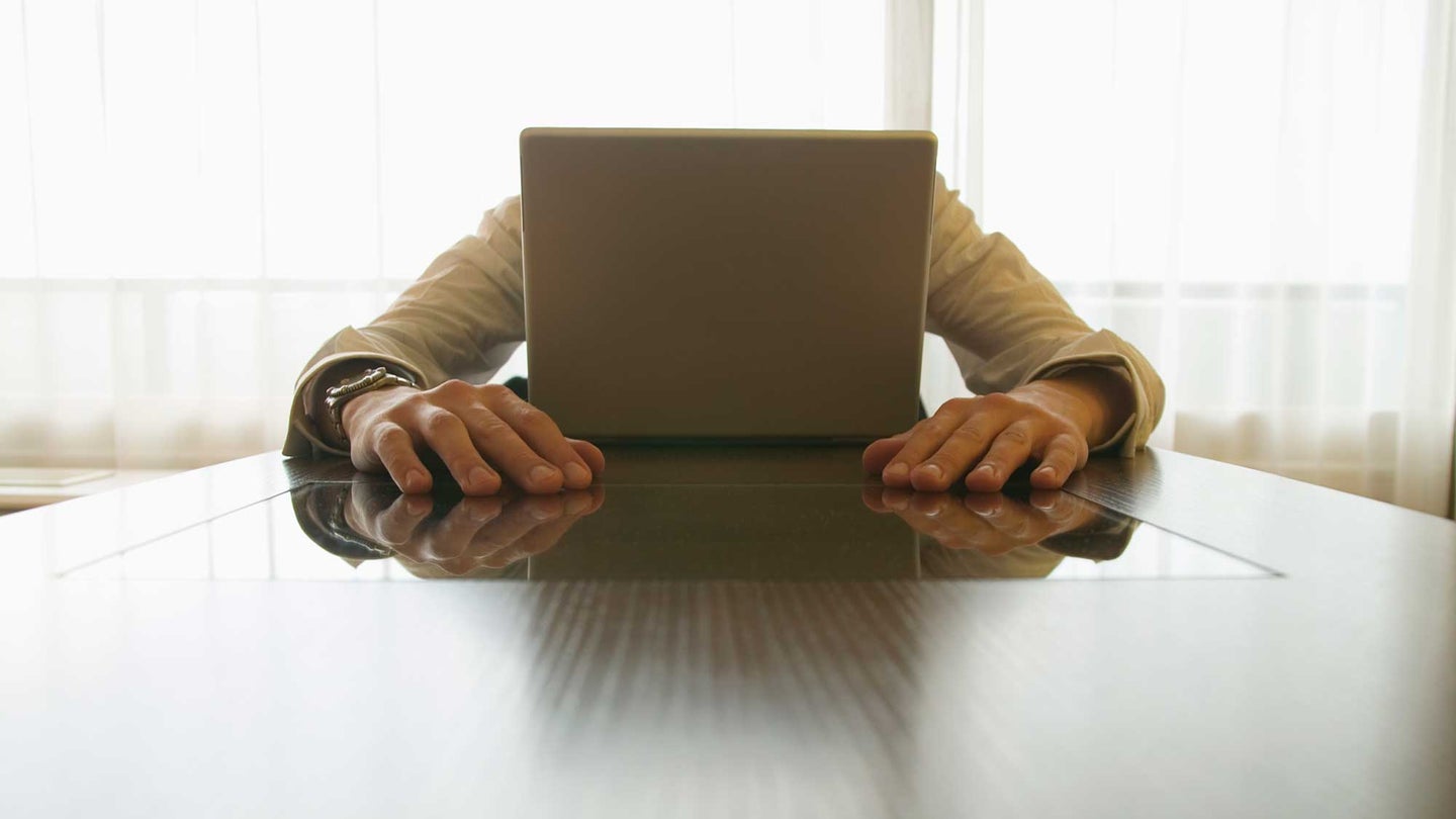 Image of hands coming out of a computer or a man hiding behind a laptop