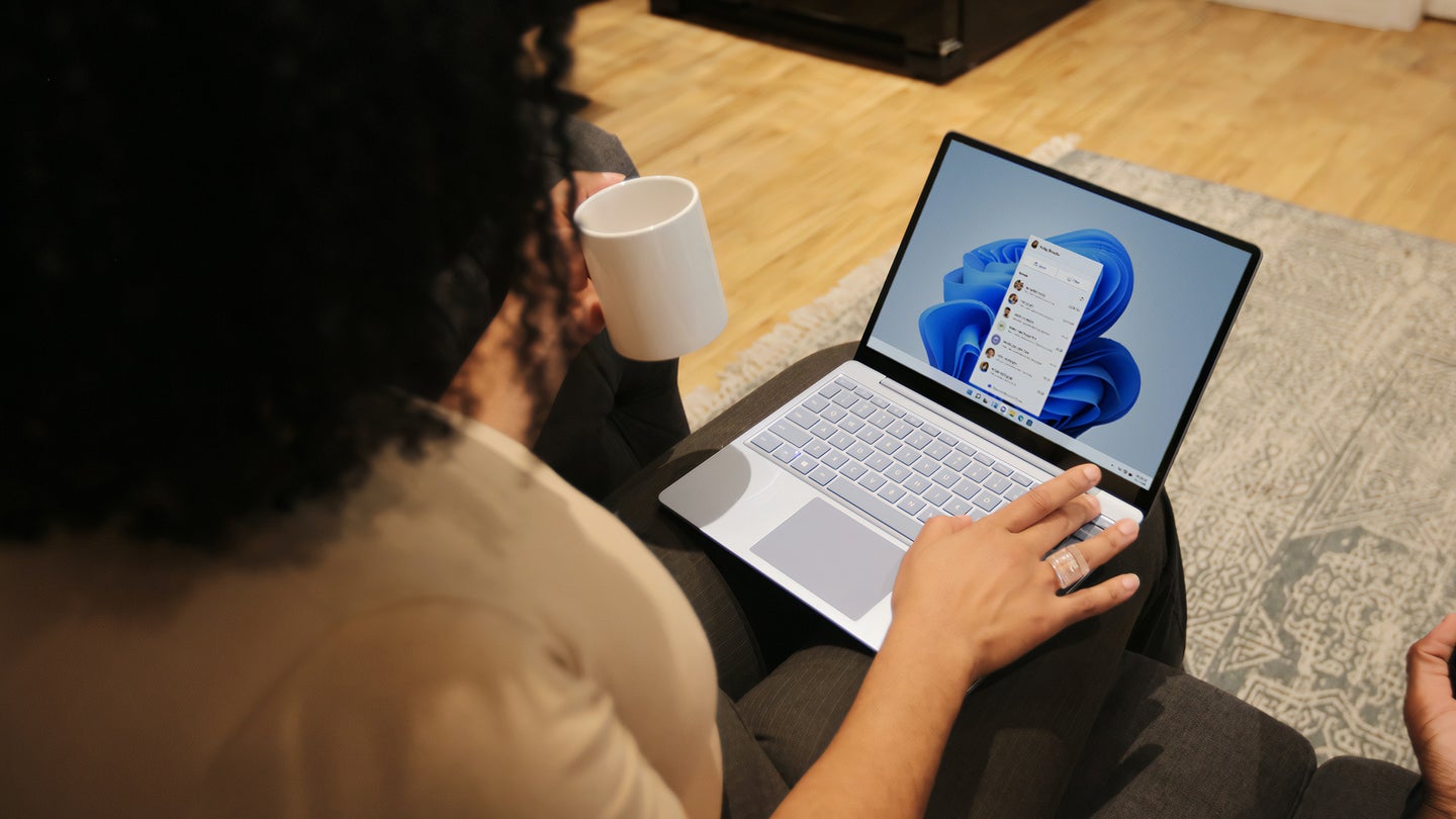 Person sitting down with a mug on one hand and the other typing on an a windows computer