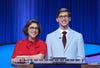 Jeopardy! host Mayim Bialik wearing red, on the left, standing next to this story's author, Jack Izzo, wearing light blue, on the right, both behind a Jeopardy! podium.