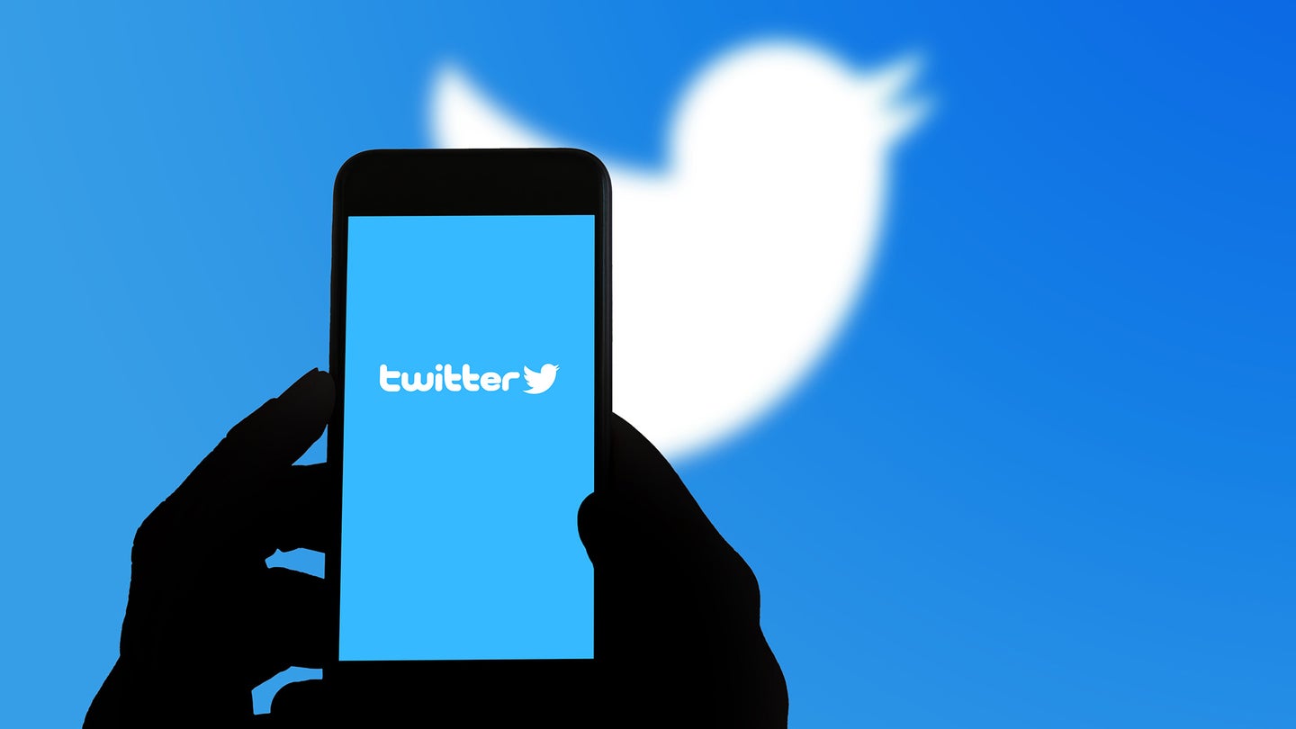 hands holding a phone with a Twitter logo on the screen. Twitter's white logo can be seen on the background.