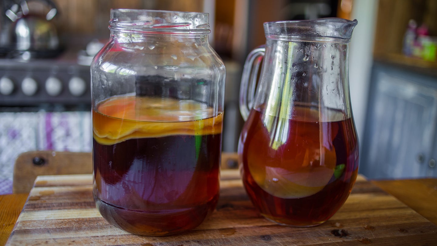 Pitcher and jar filled with kombucha on wooden kitchen counter