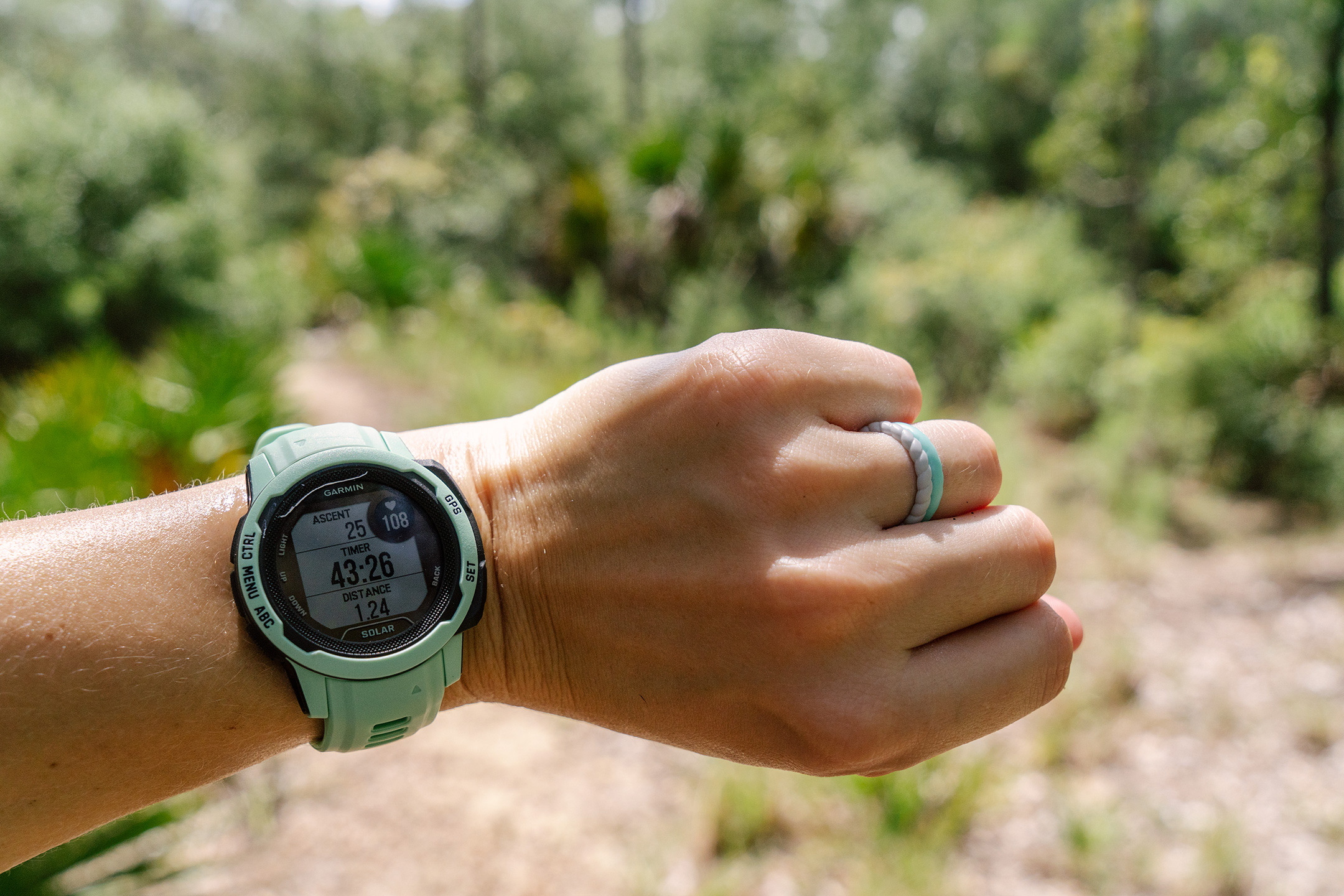 The Garmin Instinct 2S Solar fitness and smartwatch on a wrist with a forest in the background