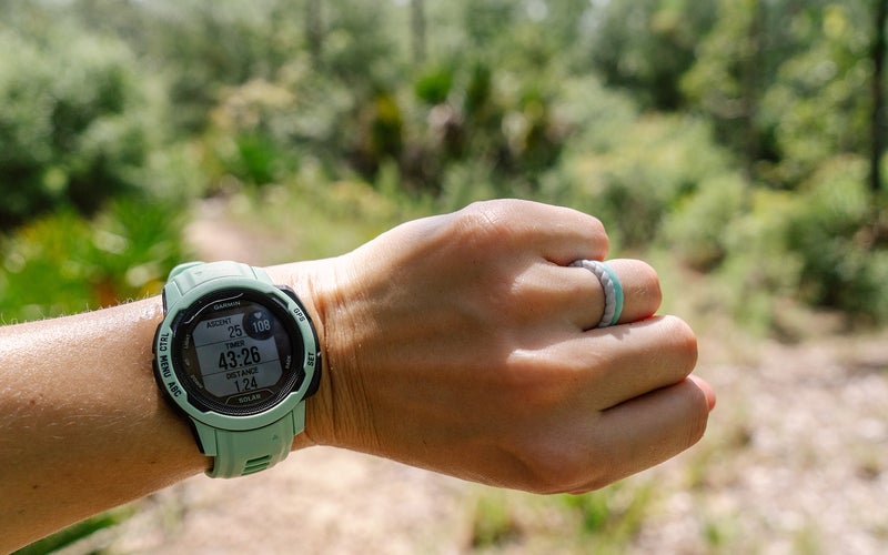 The Garmin Instinct 2S Solar fitness and smartwatch on a wrist with a forest in the background