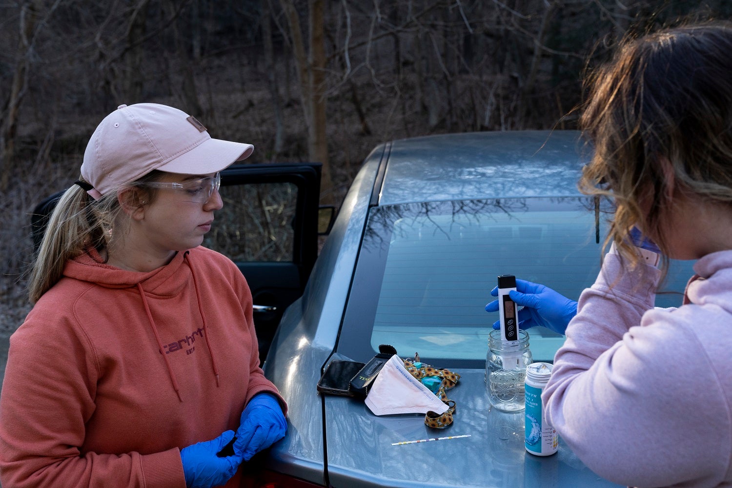 Person in pink sweatshirt and pink hat and person in pink shirt testing pH of water samples in East Palestine, Ohio