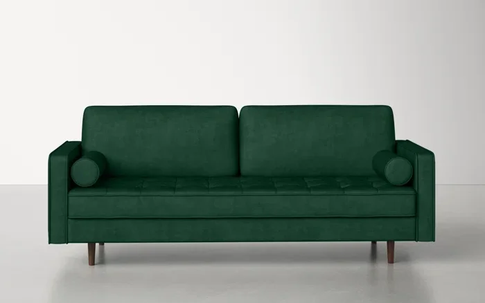 A green velvet couch on an off white floor and in front of an off white wall.