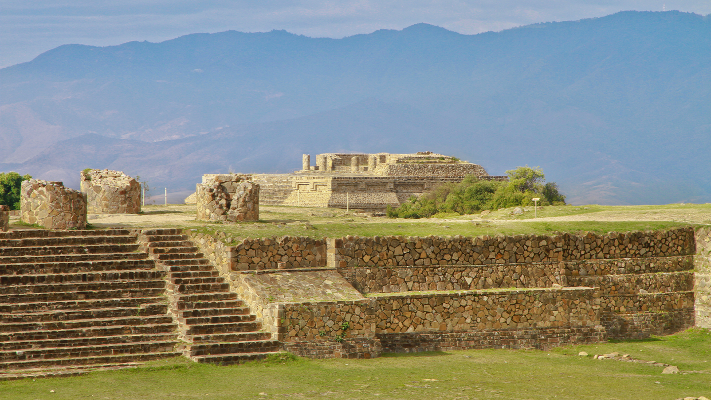 Mexico's Monte Alban archaeological site, including stone step and structures with mountains in the distance.