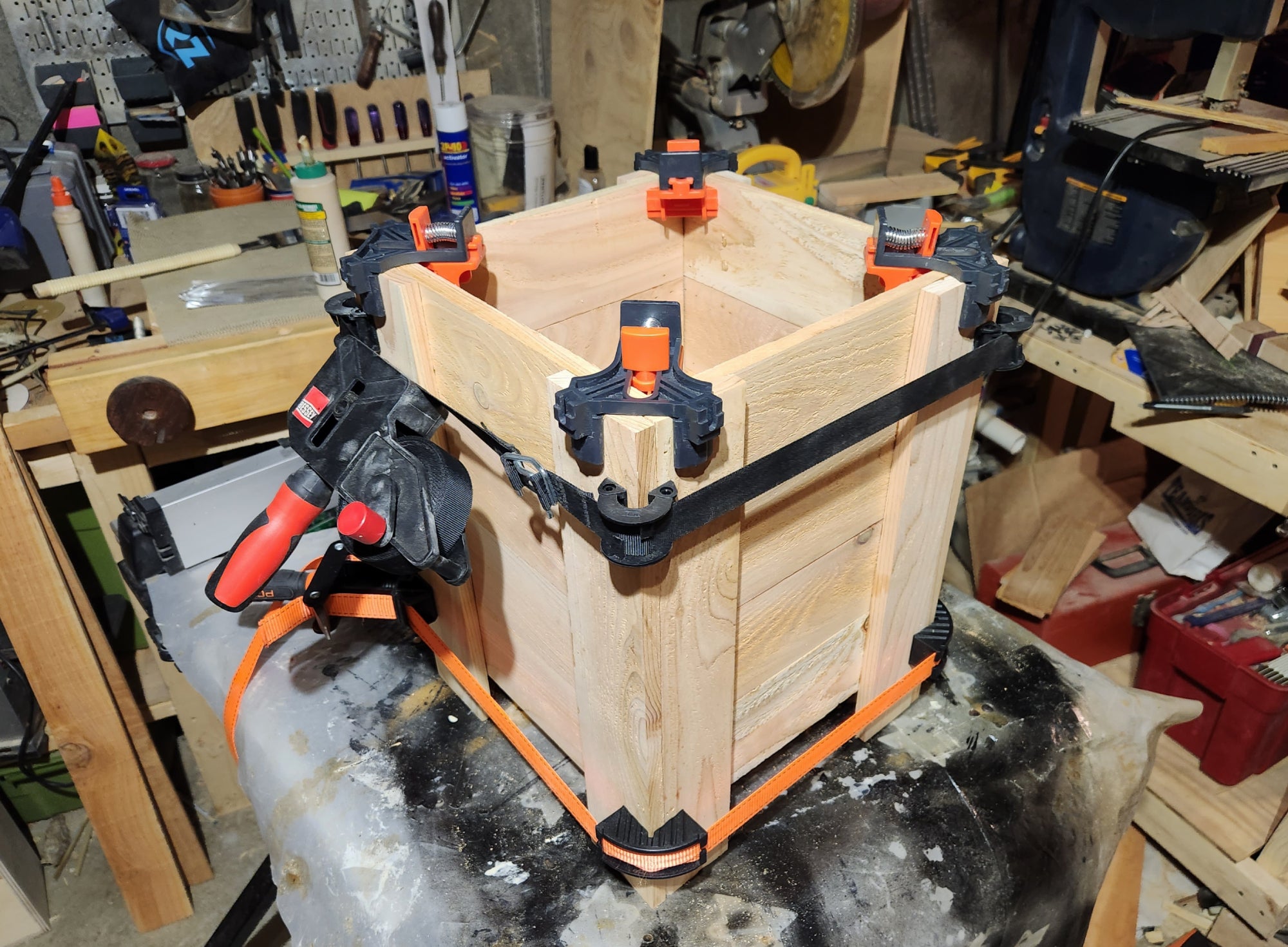 A cedar DIY planter box assembled, glued, clamped, and sitting on a table in the middle of a woodworker's shop.