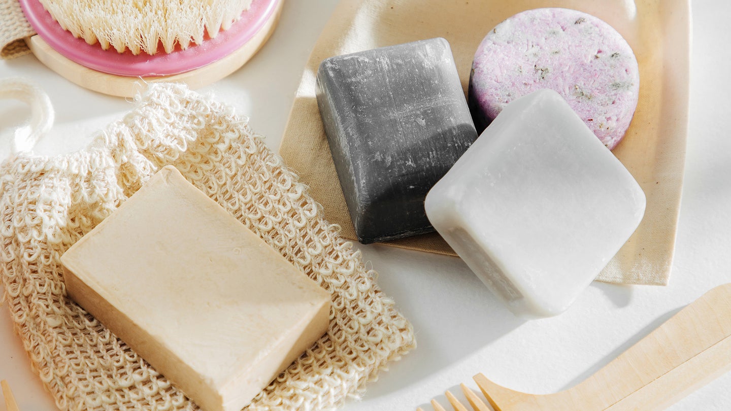 A set of hand soaps and shampoo bars over organic cotton covers and other wooden-made toiletries.