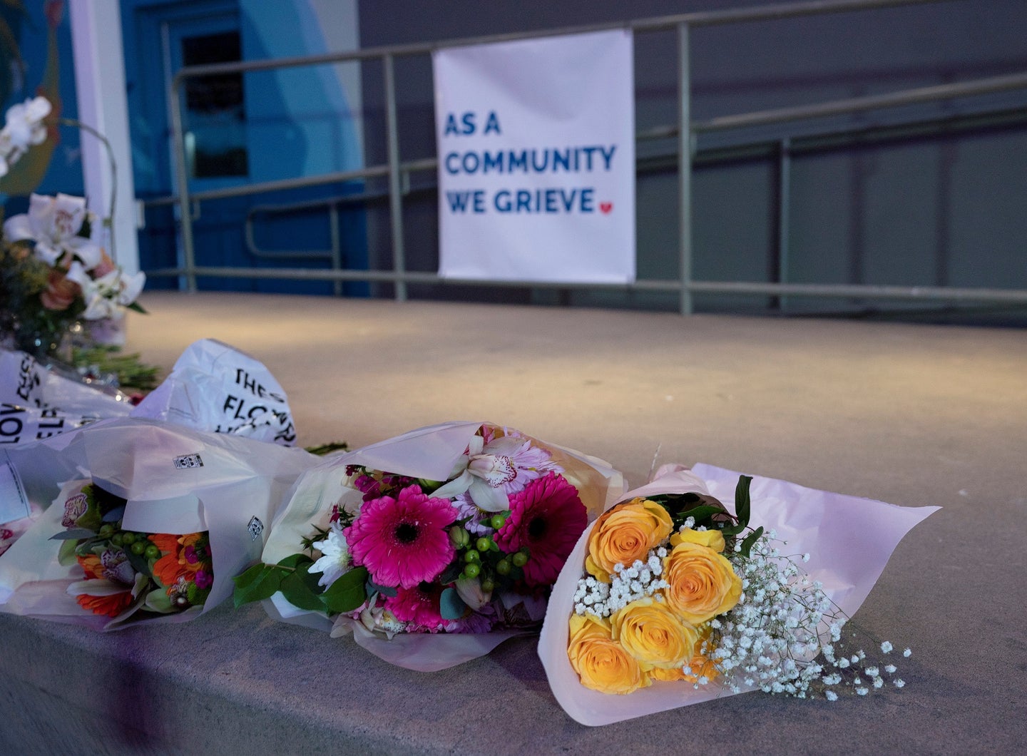 Yellow, red, and white roses left at a memorial for the victims of the Half Moon Bay mass shooting. A white sign behind the bouquets says "as a community we grieve."