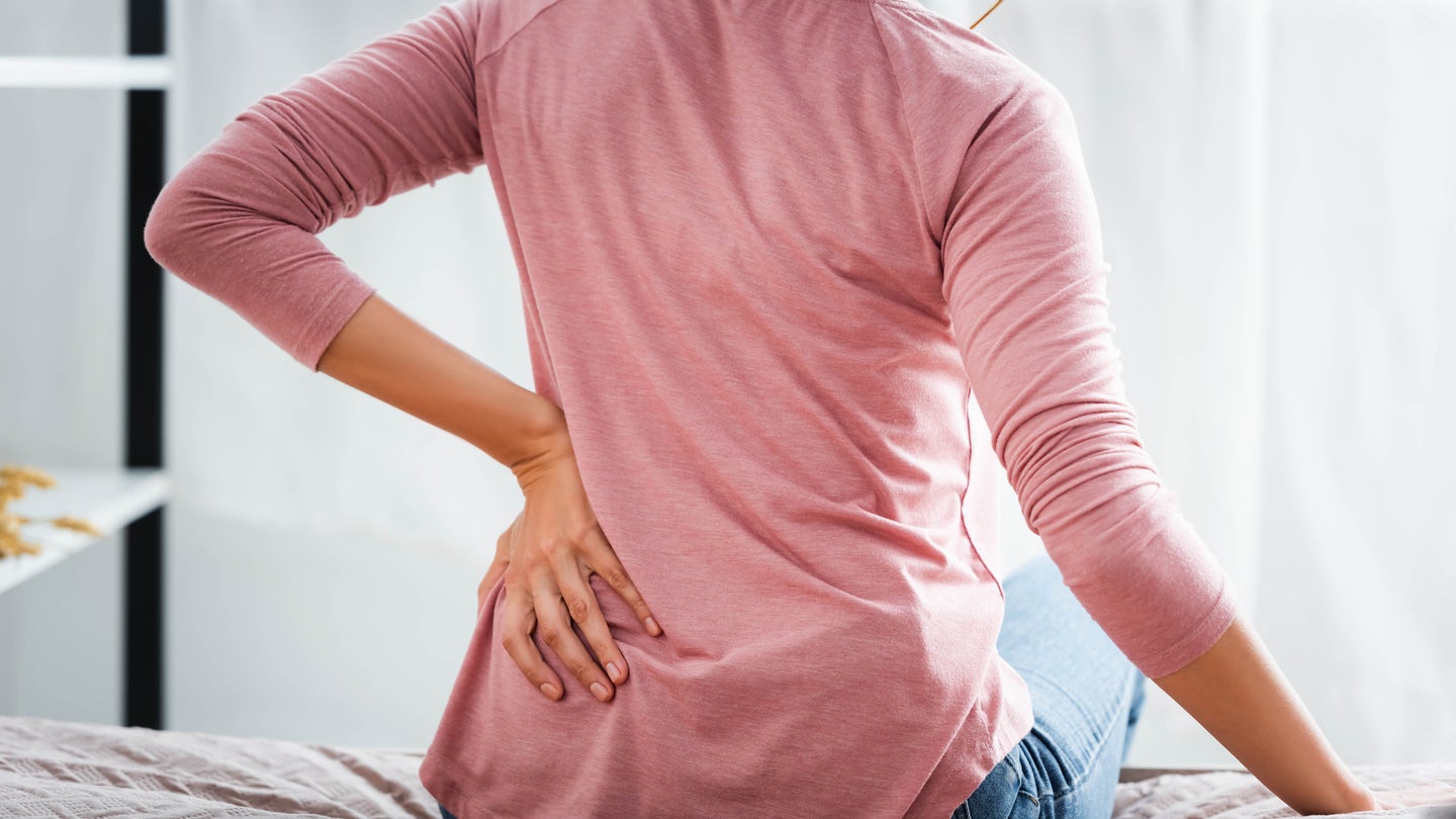 Woman sitting on bed holding lower back in pain