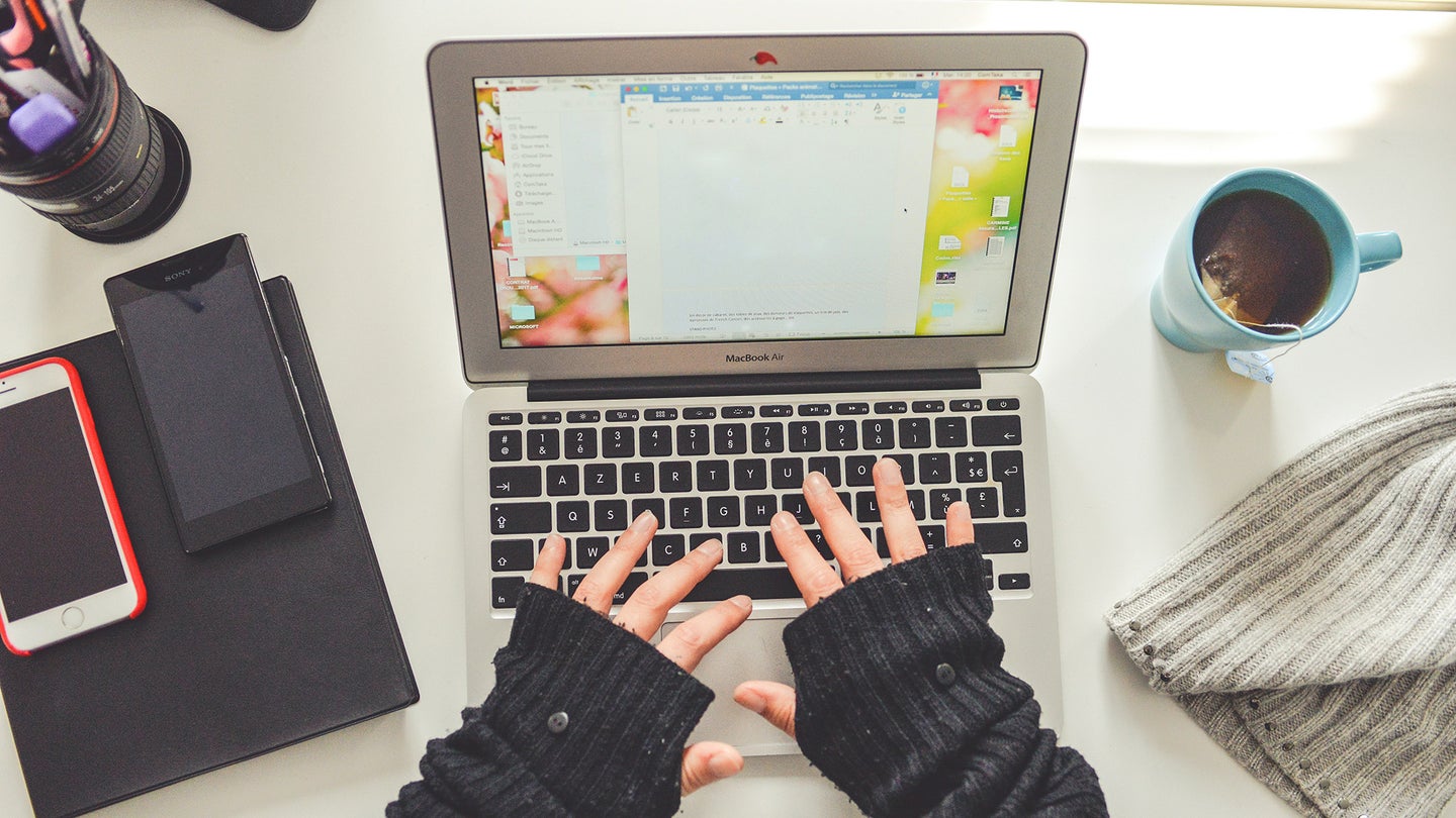 Two hands with fingerless gloves on a laptop with Microsoft Word open.