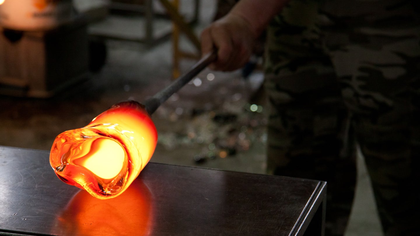Person holding handle attached to molten glass