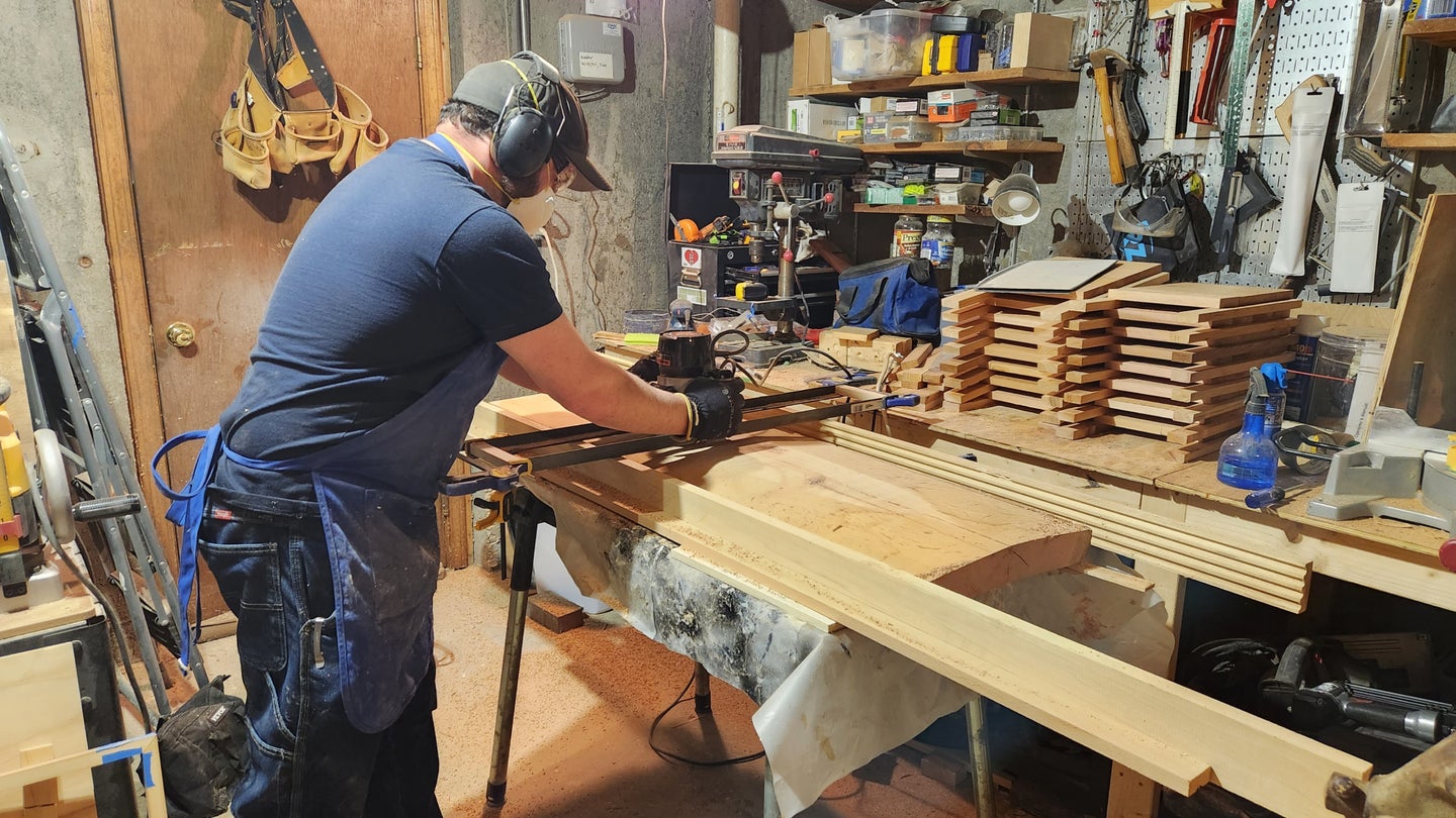 A man in a blue t-shirt and jeans working with a DIY router sled in a woodshop.