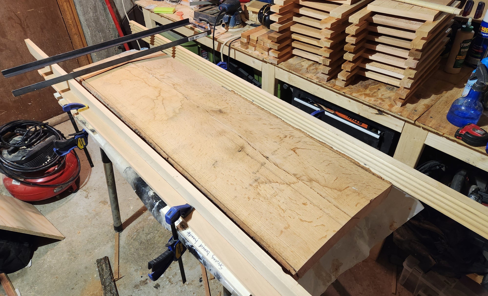 The two rails of a DIY router sled set up around a large, curved board in a woodshop.