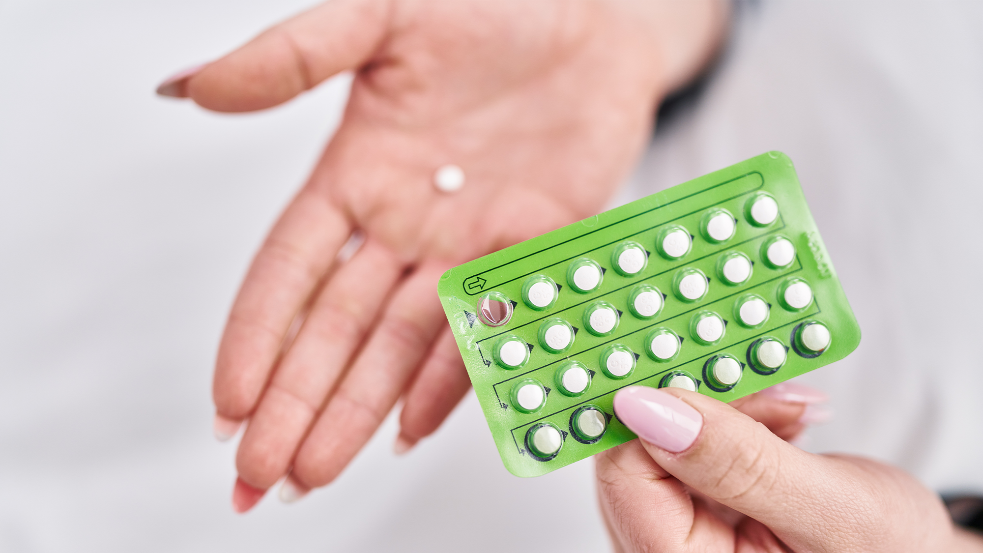 A woman holes a pack of birth control pills in one hand, with a single pill in the other.