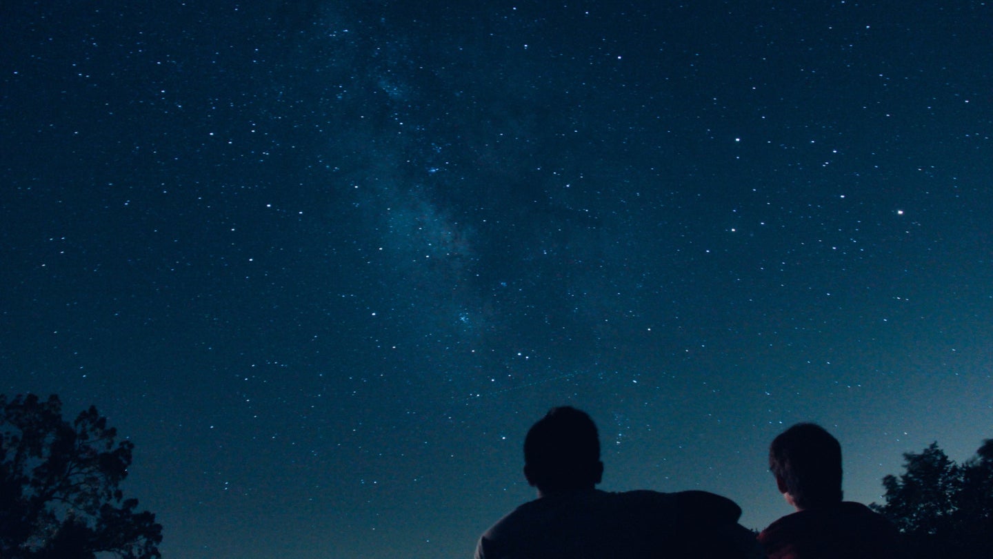 Two people, silhouetted, looking up at a clear night sky.